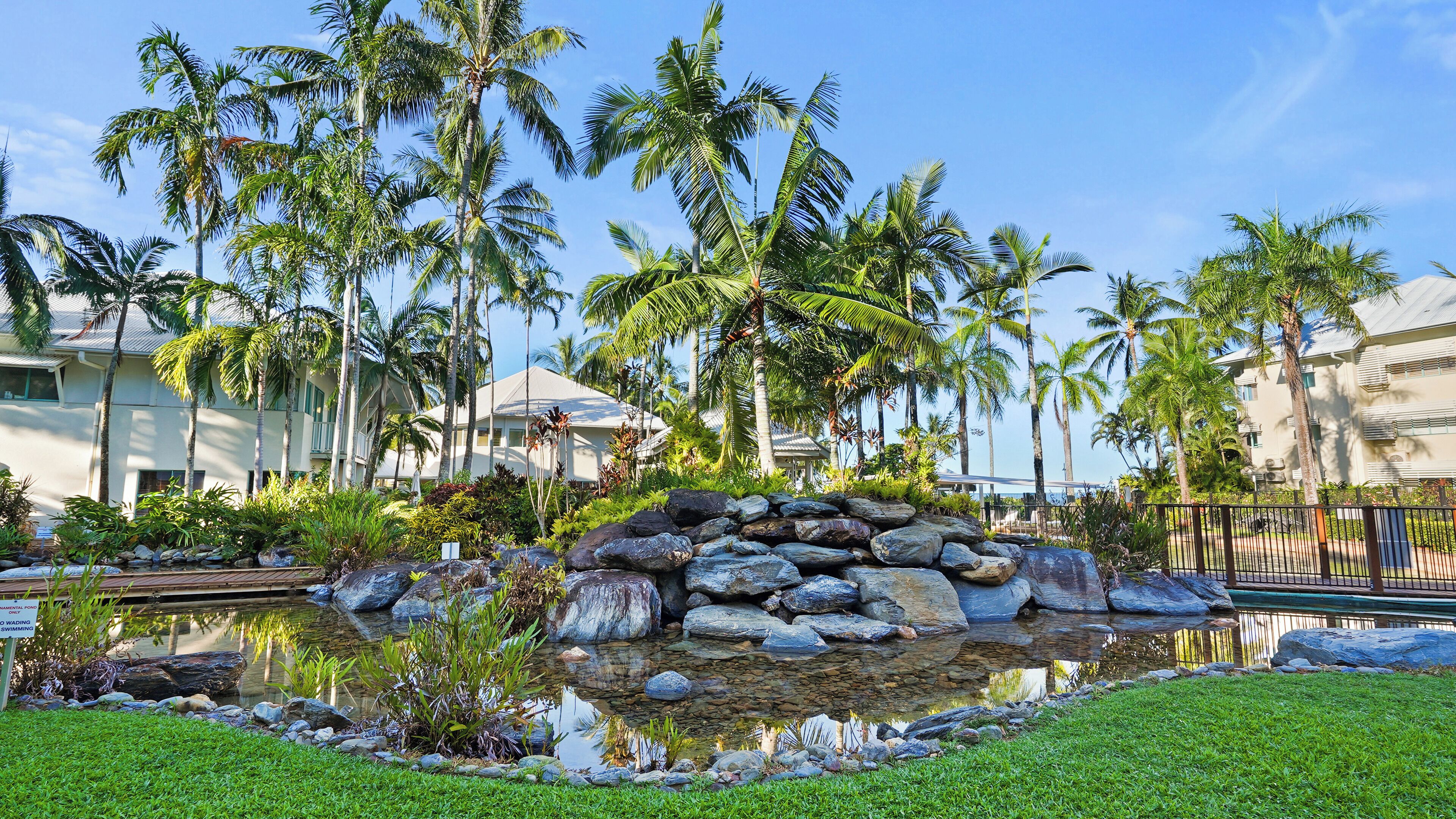 A tropical resort with a pond, palm trees, and a stone wall.