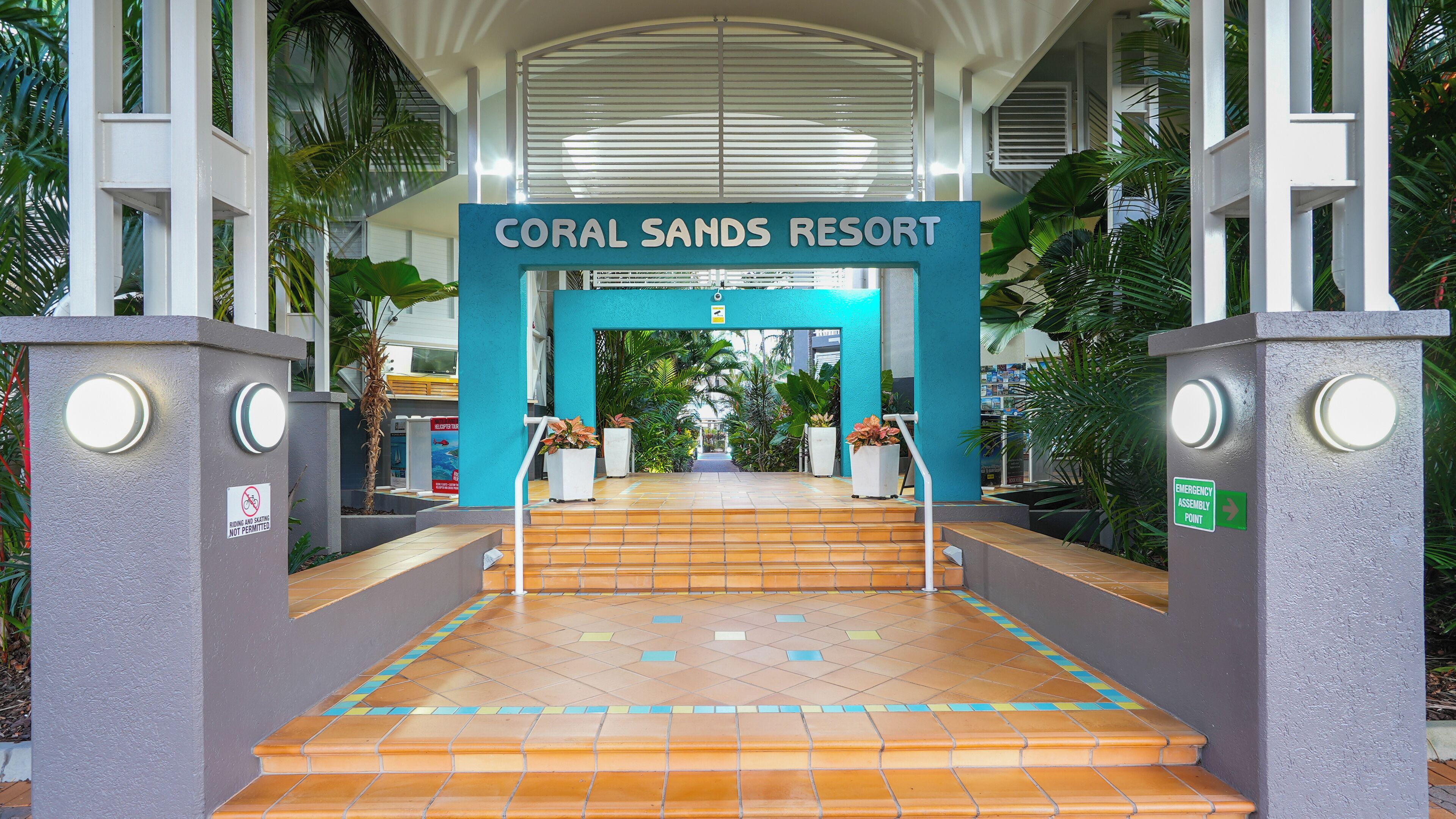 The entrance to Coral Sands Resort with a blue sign, tiled steps, and surrounding greenery.