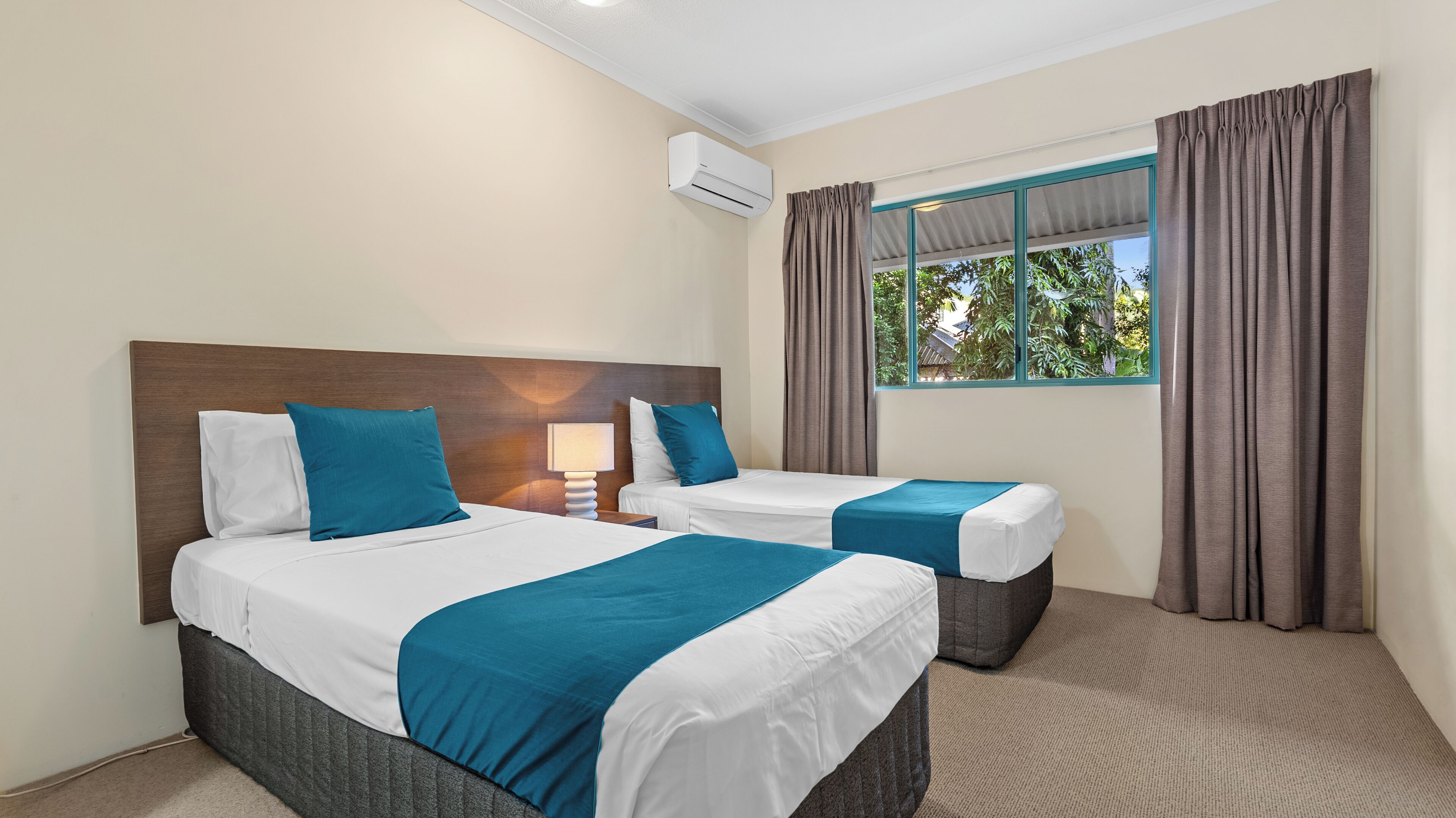 Habitación de hotel con dos camas, una ventana con cortinas, un equipo de aire acondicionado y una lámpara.