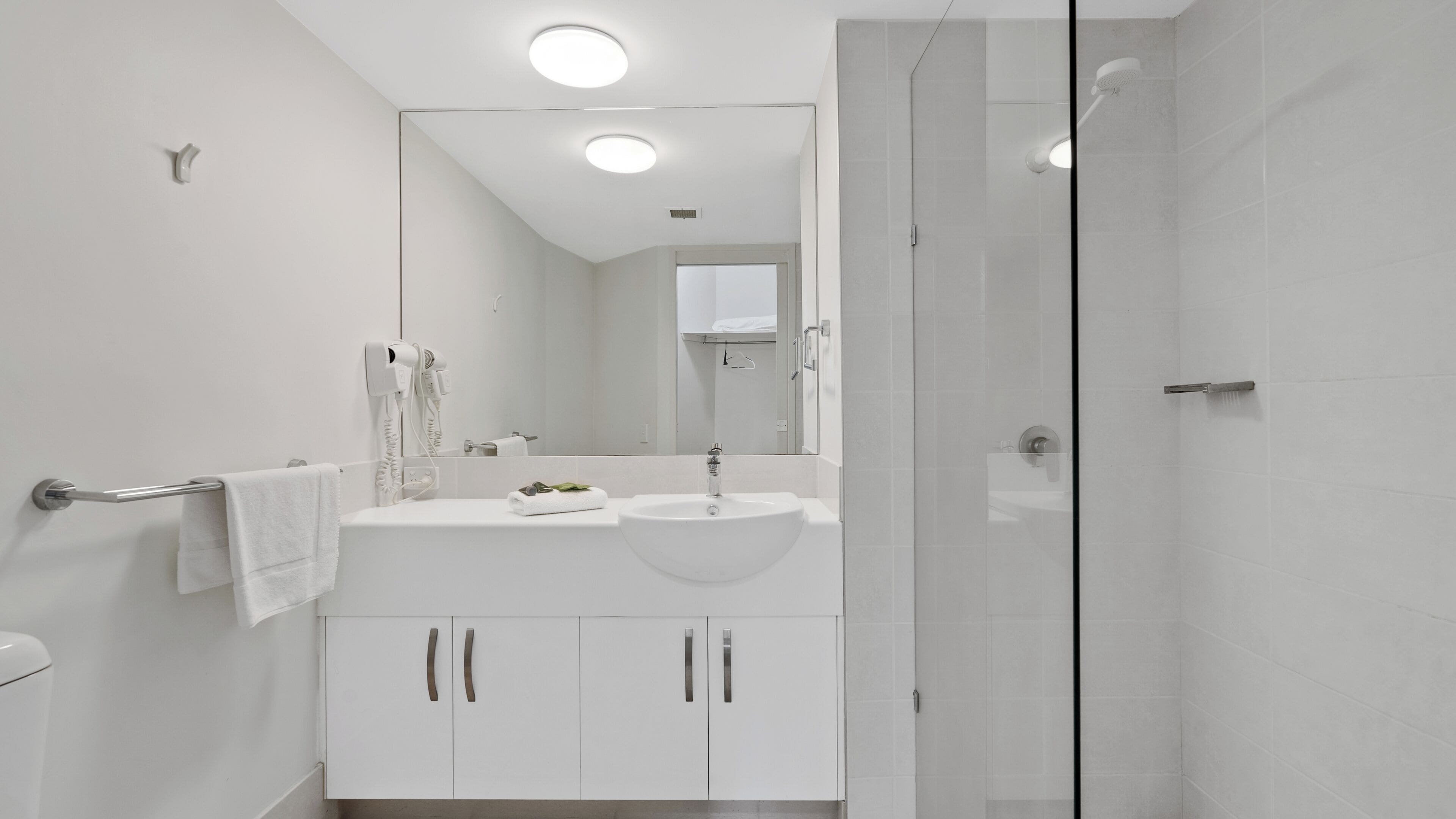 A modern bathroom with a white sink, vanity, and a glass shower enclosure.