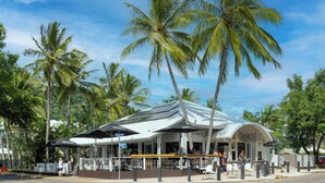 A beachside restaurant with outdoor seating, palm trees, and a covered patio area.