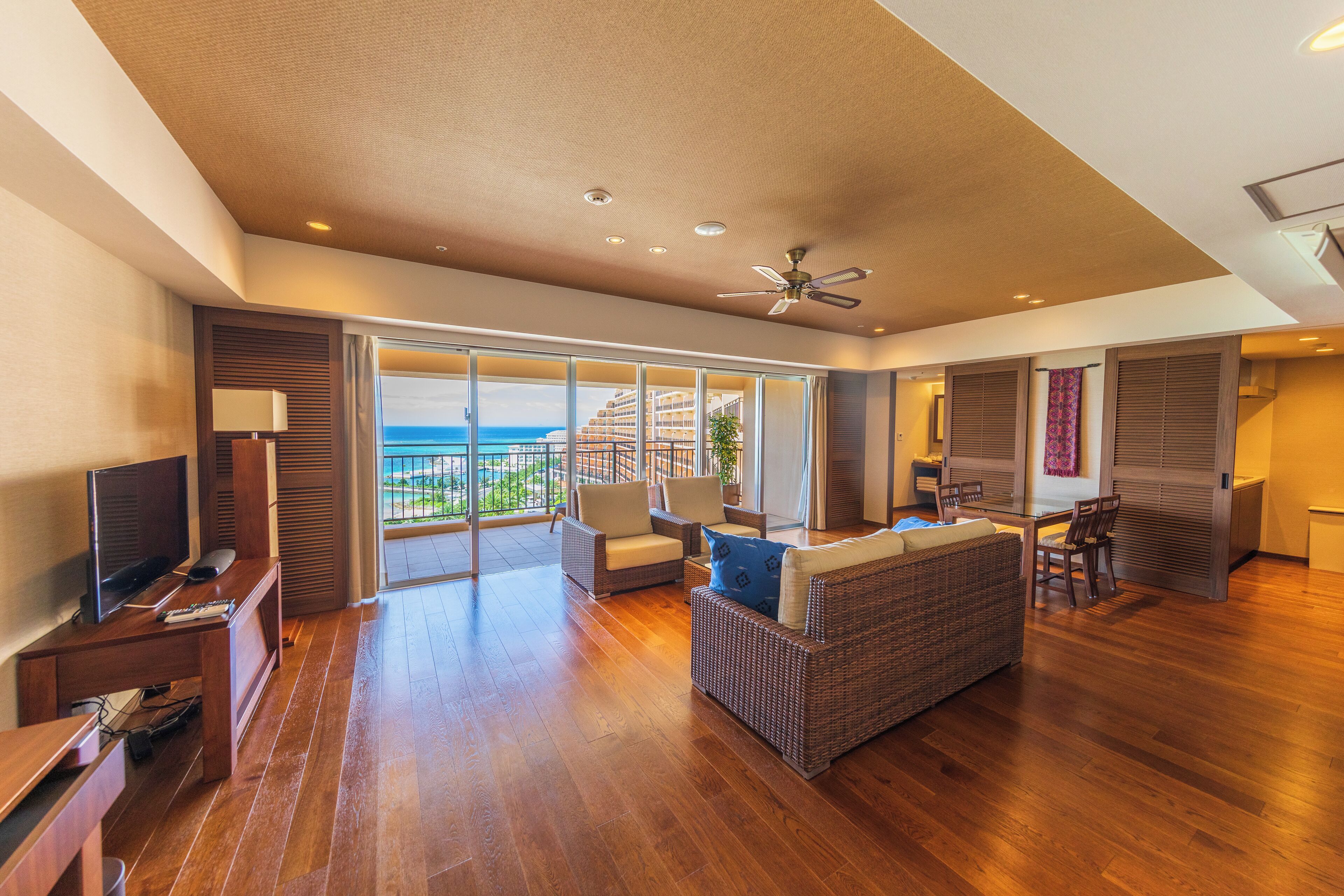 A spacious living area with a large window offering a view of the ocean, a ceiling fan, and a dining area with a table and chairs.