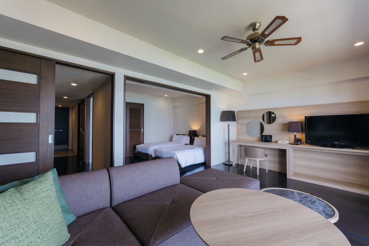 Een moderne hotelkamer met een bank, een ronde tafel, een bed, een bureau met een televisie en een plafondventilator.