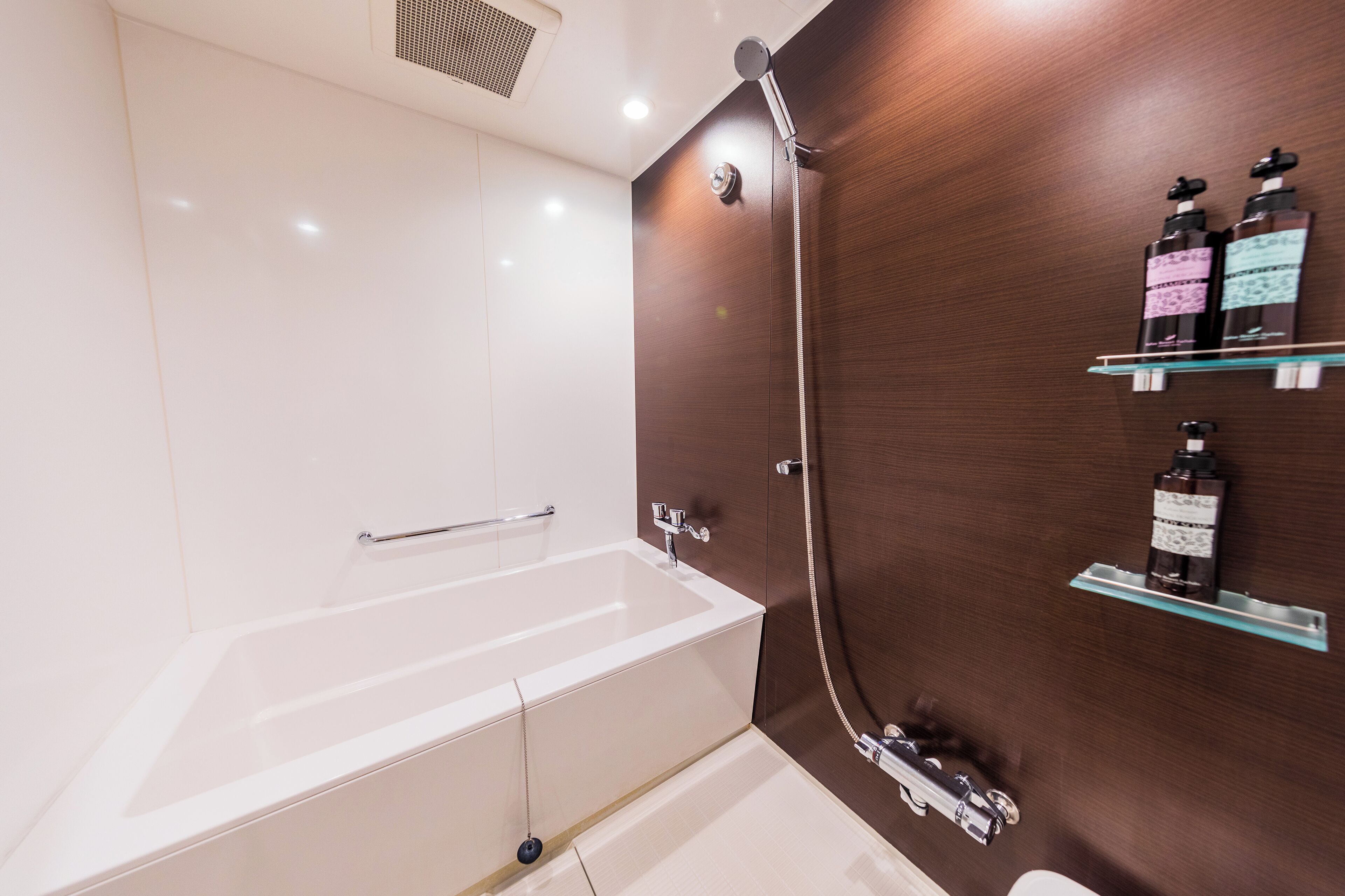 A modern bathroom with a bathtub, a shower, and a glass shelf with toiletries.