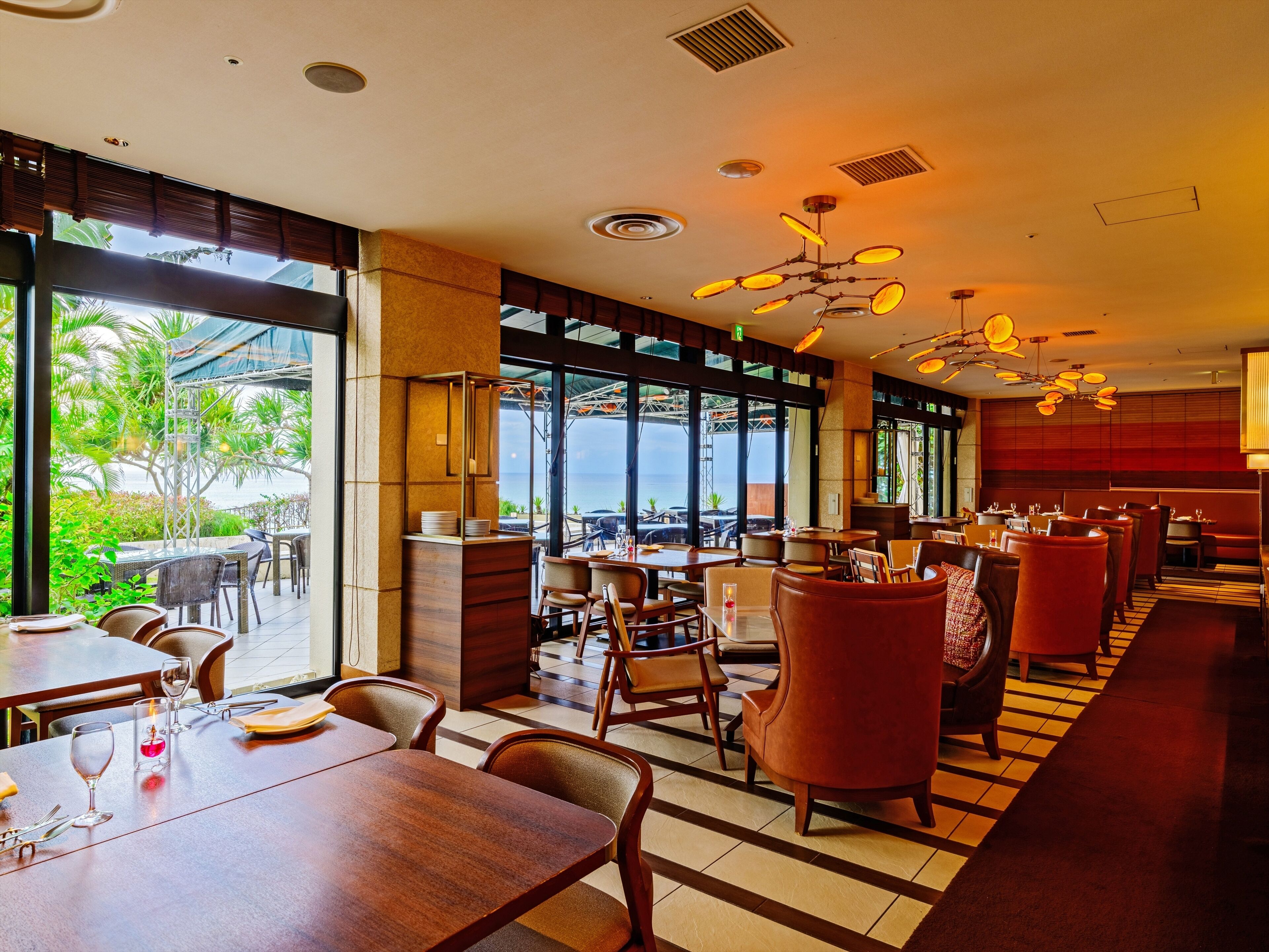 Un restaurante con vista al océano, con mesas y sillas de madera, una zona de bar y amplias ventanas.
