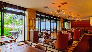 Un restaurant offrant une vue sur l’océan, avec des tables et des chaises en bois, un bar et de grandes fenêtres.