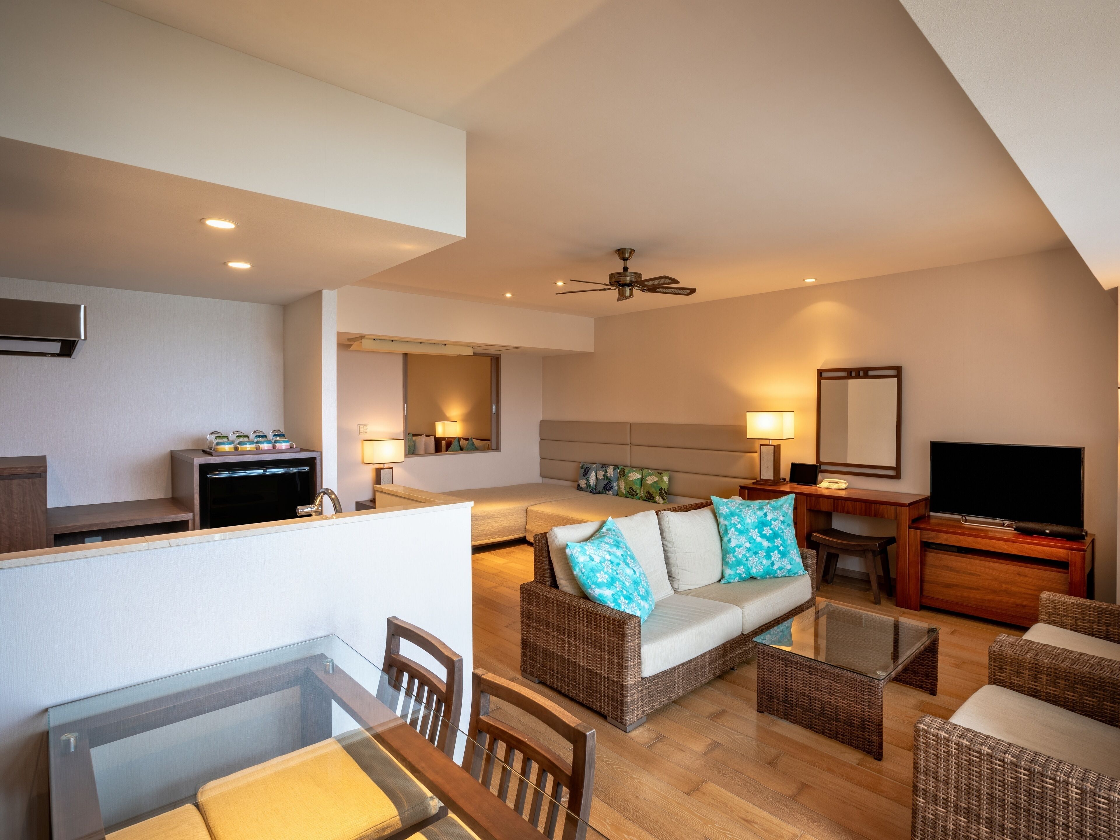 A modern hotel room with a dining area, a sofa set, a flat-screen TV, and a ceiling fan.