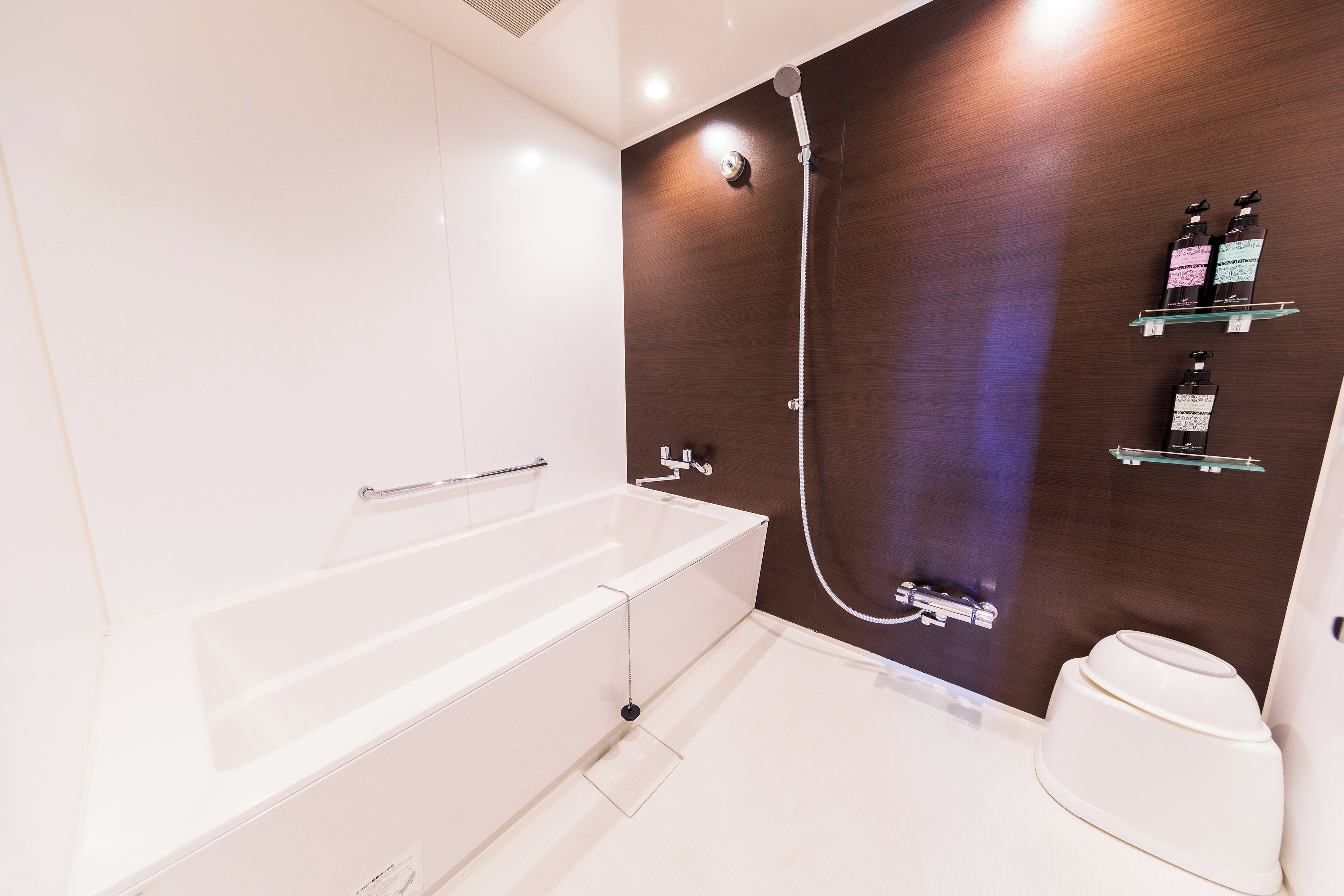 Un baño moderno con una bañera blanca, ducha e inodoro. Hay dos estantes con artículos de aseo.