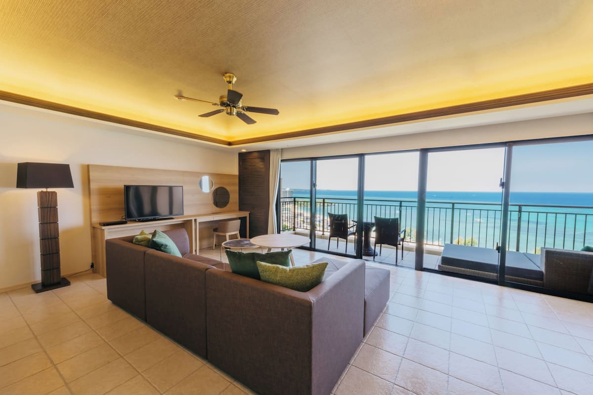 Een moderne woonkamer met een bank, televisie en een balkon met uitzicht op zee.