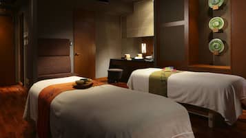 Two single beds with white linens and throw blankets, a wooden table, and a large mirror adorn this stylish room with a city view.