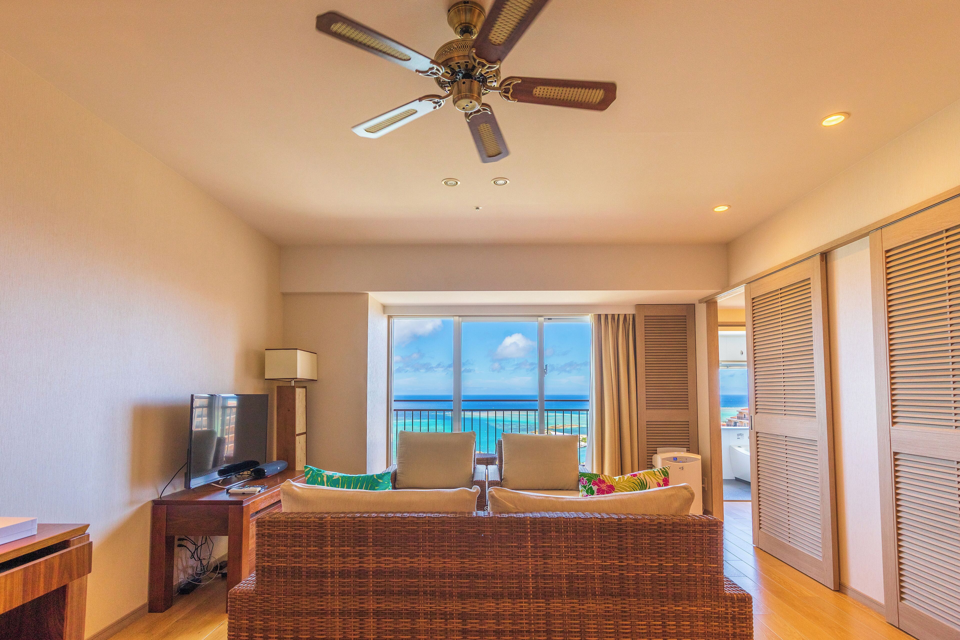 A hotel room with a balcony, a television, a desk, and a bed with pillows.