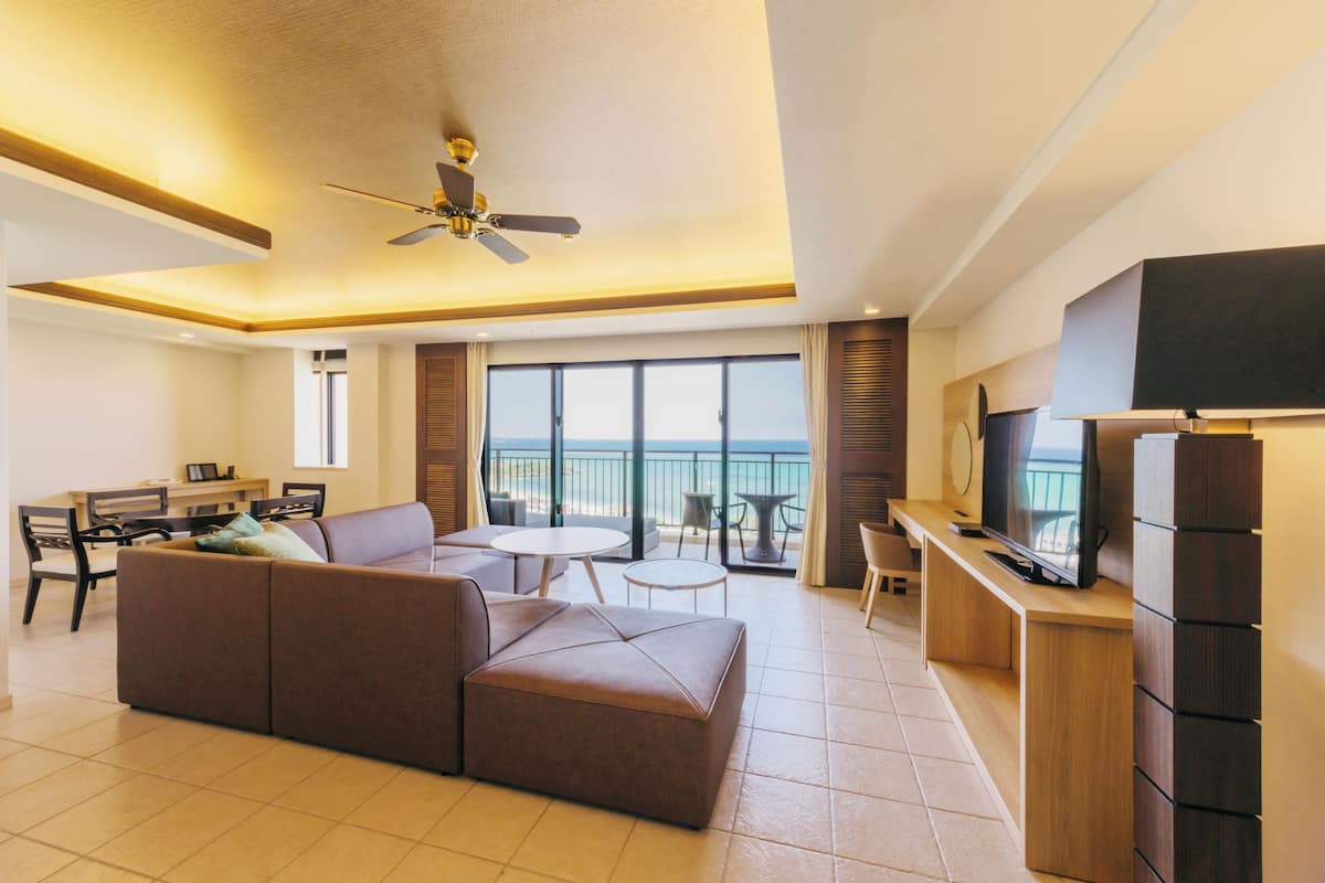 Een moderne hotelkamer met een grote bank, een eettafel, een televisie en een balkon met uitzicht.