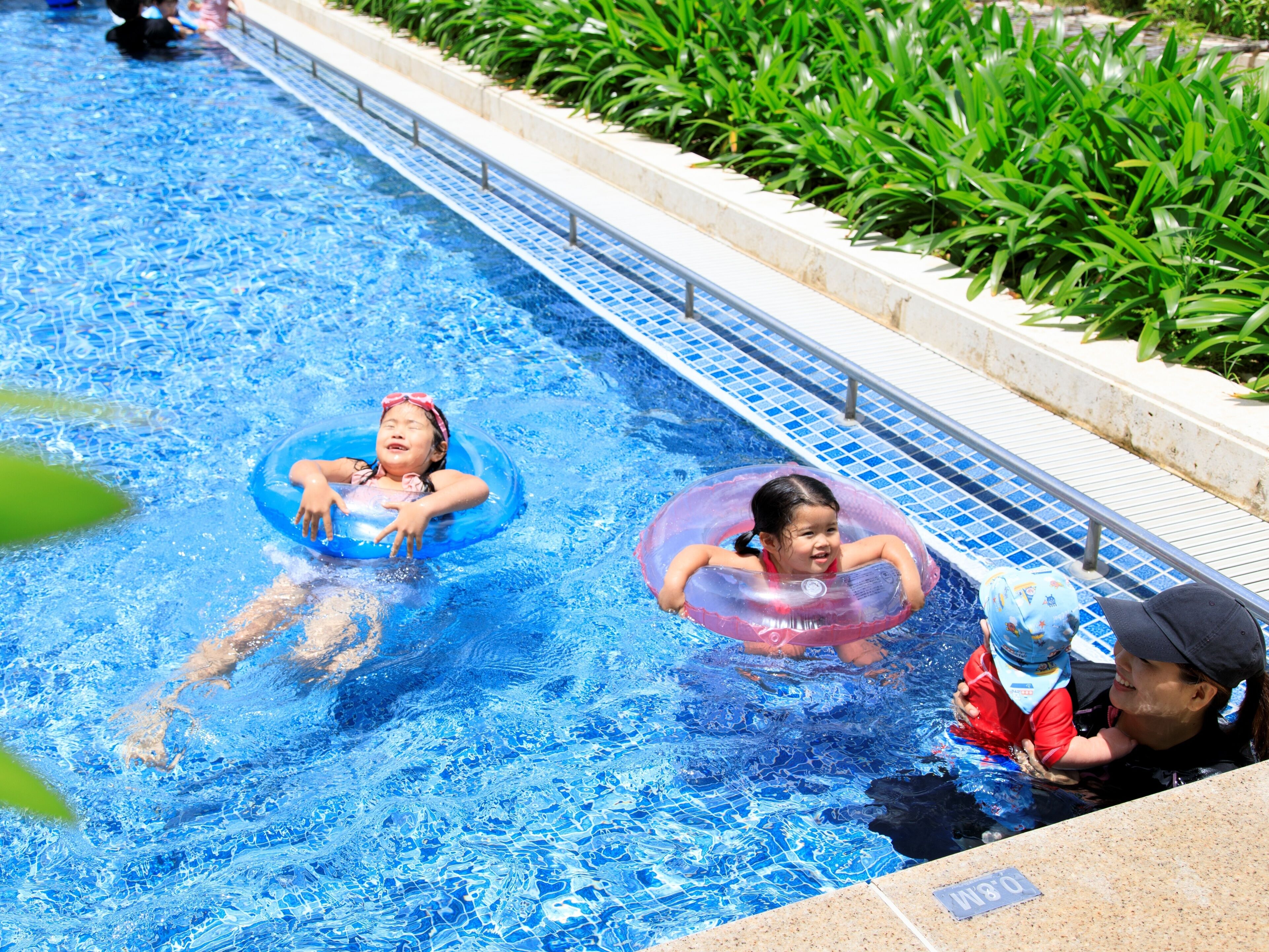 A swimming pool with two children in inflatable rings and an adult supervising.