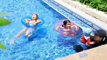 A swimming pool with two children in inflatable rings and an adult supervising.