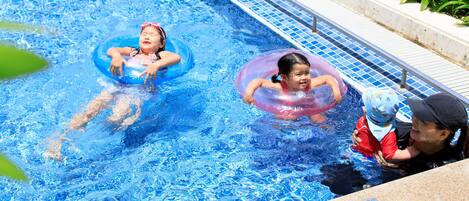 A swimming pool with two children in inflatable rings and an adult supervising.