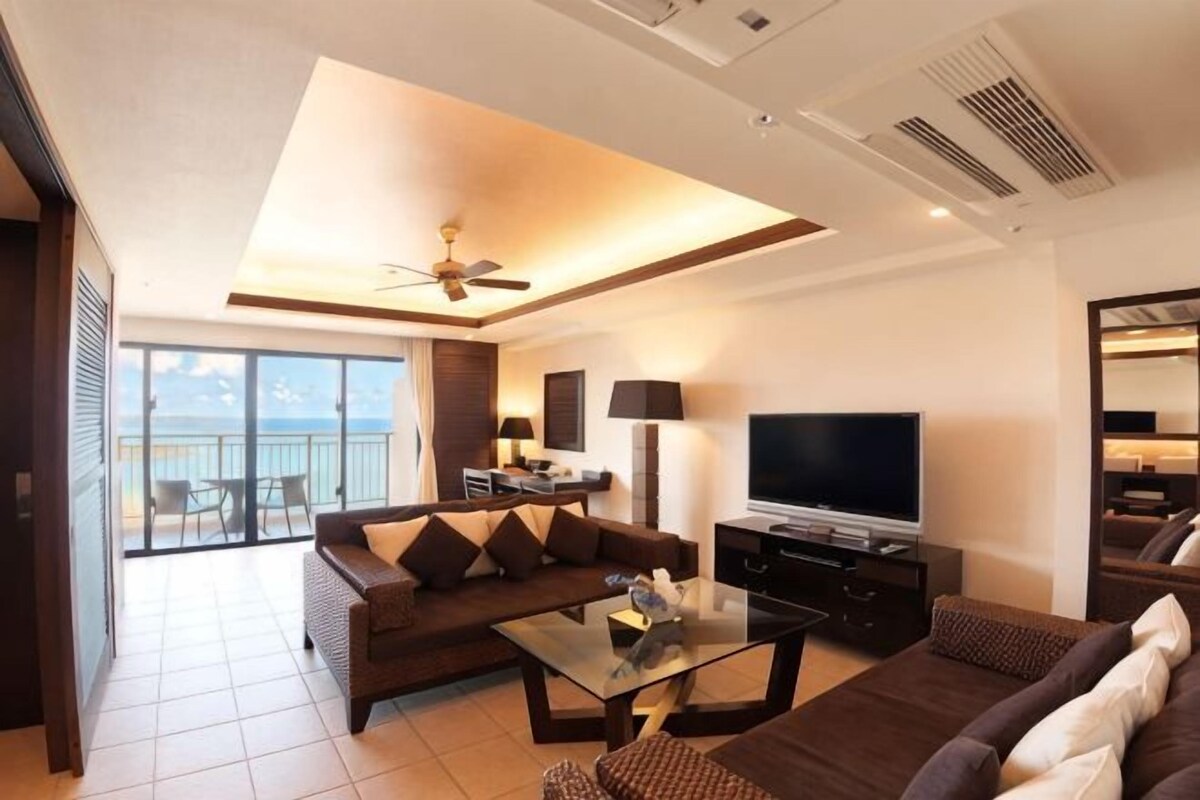 Ein modernes Wohnzimmer mit einer Couch, einem Couchtisch, einem Fernseher und Blick auf einen Balkon.