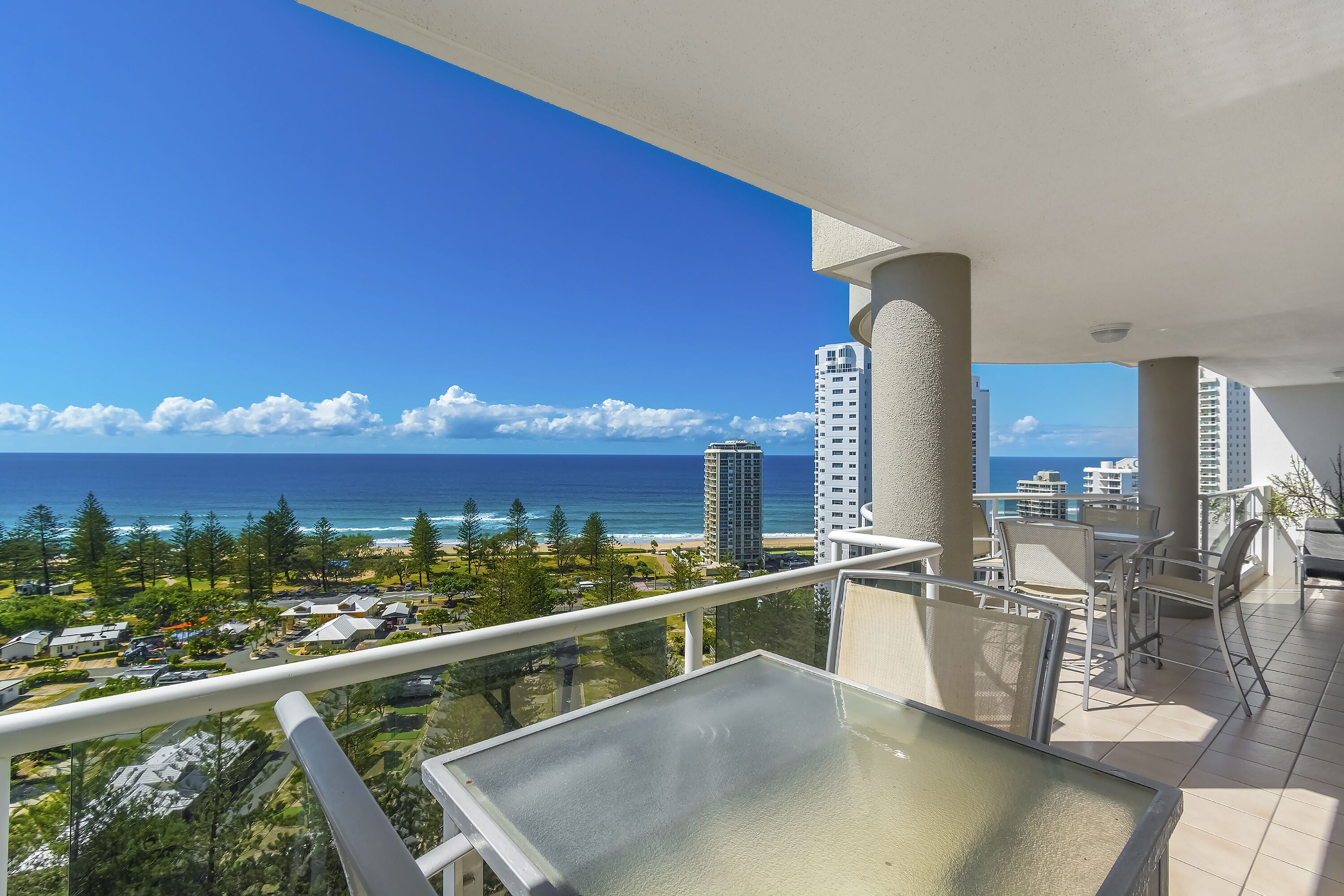 Un balcon offrant une vue dégagée sur l’océan et la plage, entouré d’immeubles imposants et de verdure.