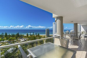 Un balcon offrant une vue dégagée sur l’océan et la plage, entouré d’immeubles imposants et de verdure.