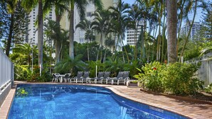 A swimming pool with a tiled edge, surrounded by palm trees and a brick deck. - Oscar on Main Resort (Main Beach)