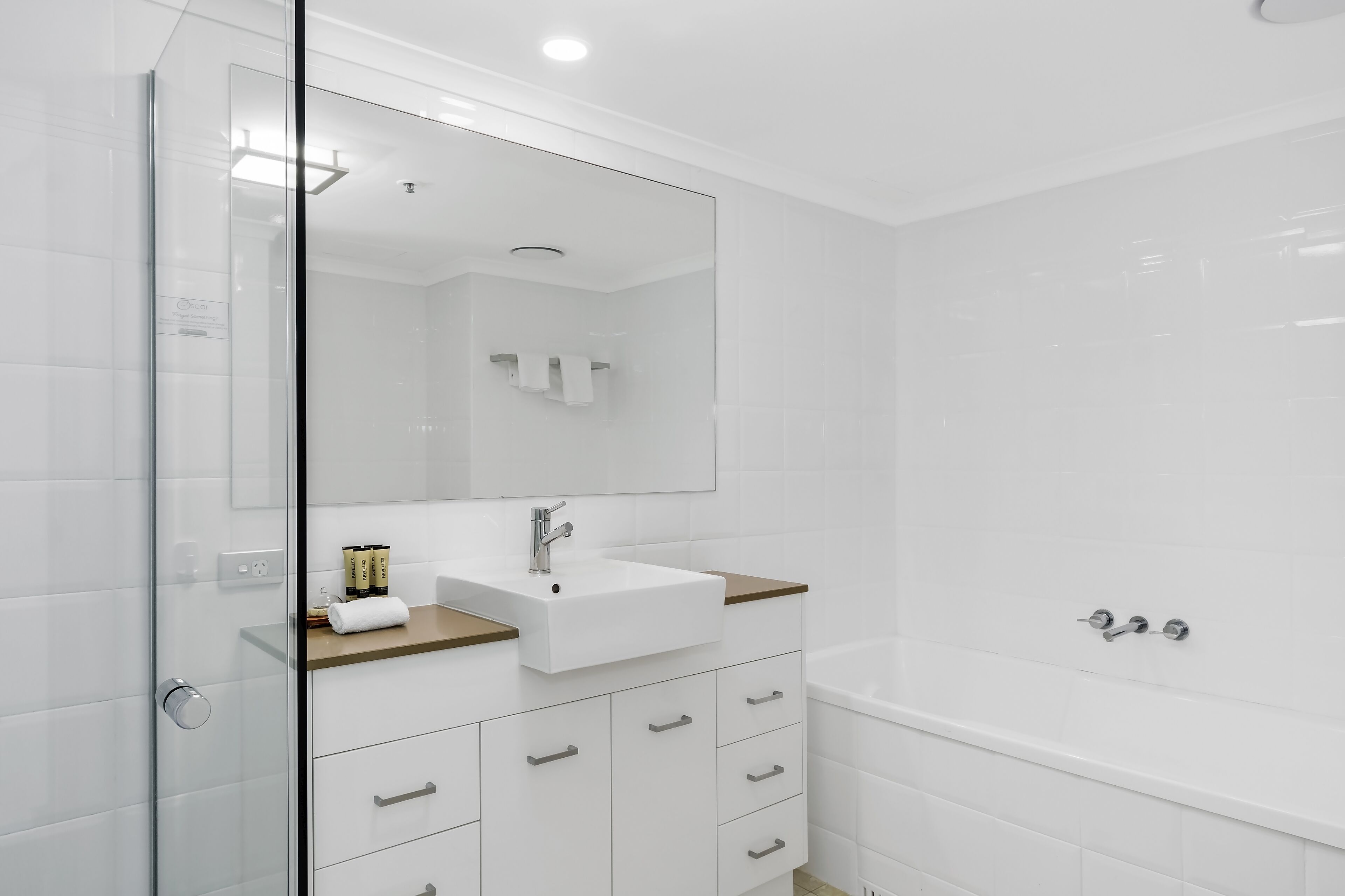 A modern bathroom with a glass shower enclosure, a white sink with a wooden countertop, and a bathtub.
