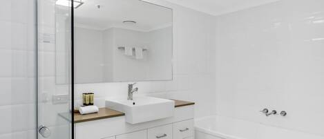 A modern bathroom with a glass shower enclosure, a white sink with a wooden countertop, and a bathtub.