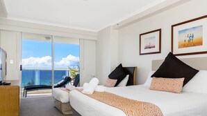 A hotel room with a bed, a desk, a chair, and a balcony with a view of the ocean. - Oscar on Main Resort (Main Beach)