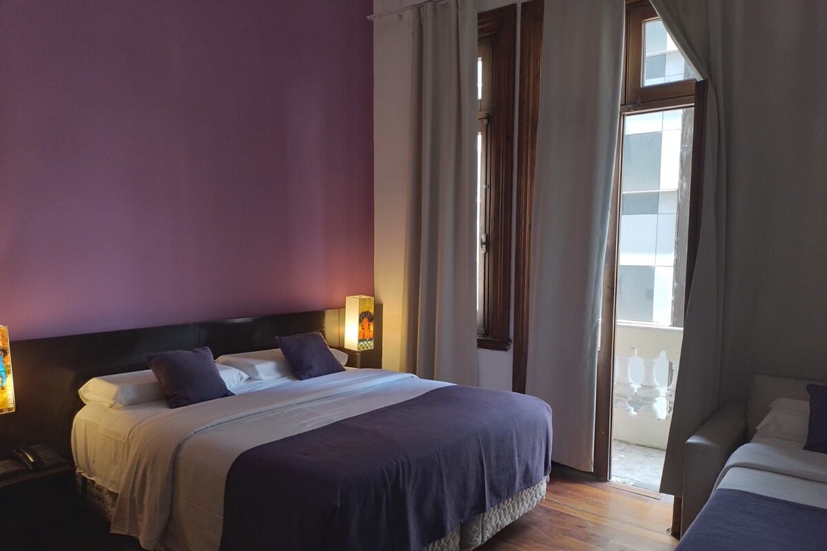 Ein Hotelzimmer mit einem Bett, Nachttischlampen, einem Beistelltisch und Blick ins Freie.