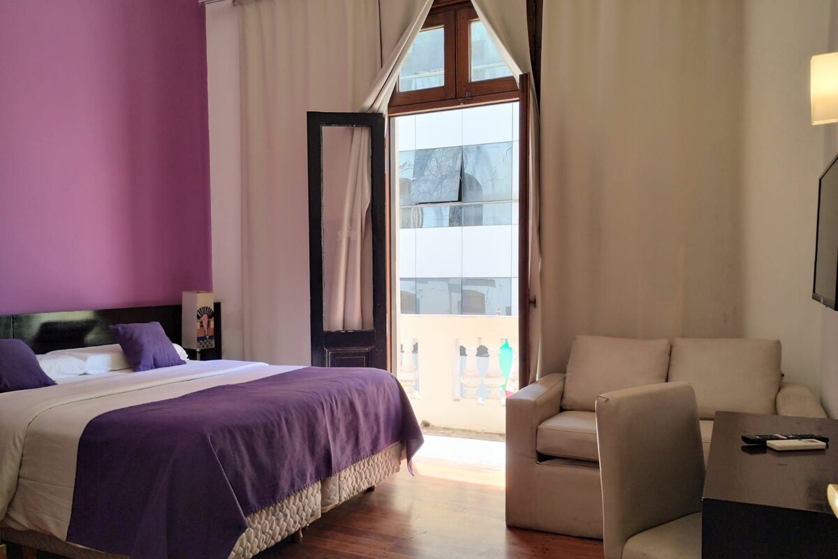 Ein Schlafzimmer mit Bett, Stuhl, Schreibtisch und einem Fenster mit Vorhängen.