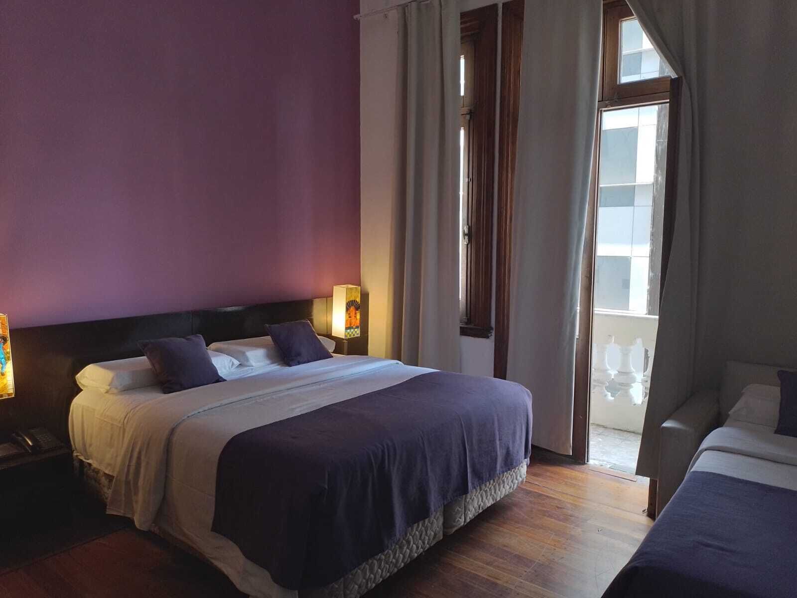 Hotellihuone, jossa on sänky, yöpöytälamput, yöpöytä ja näkymä ulos.