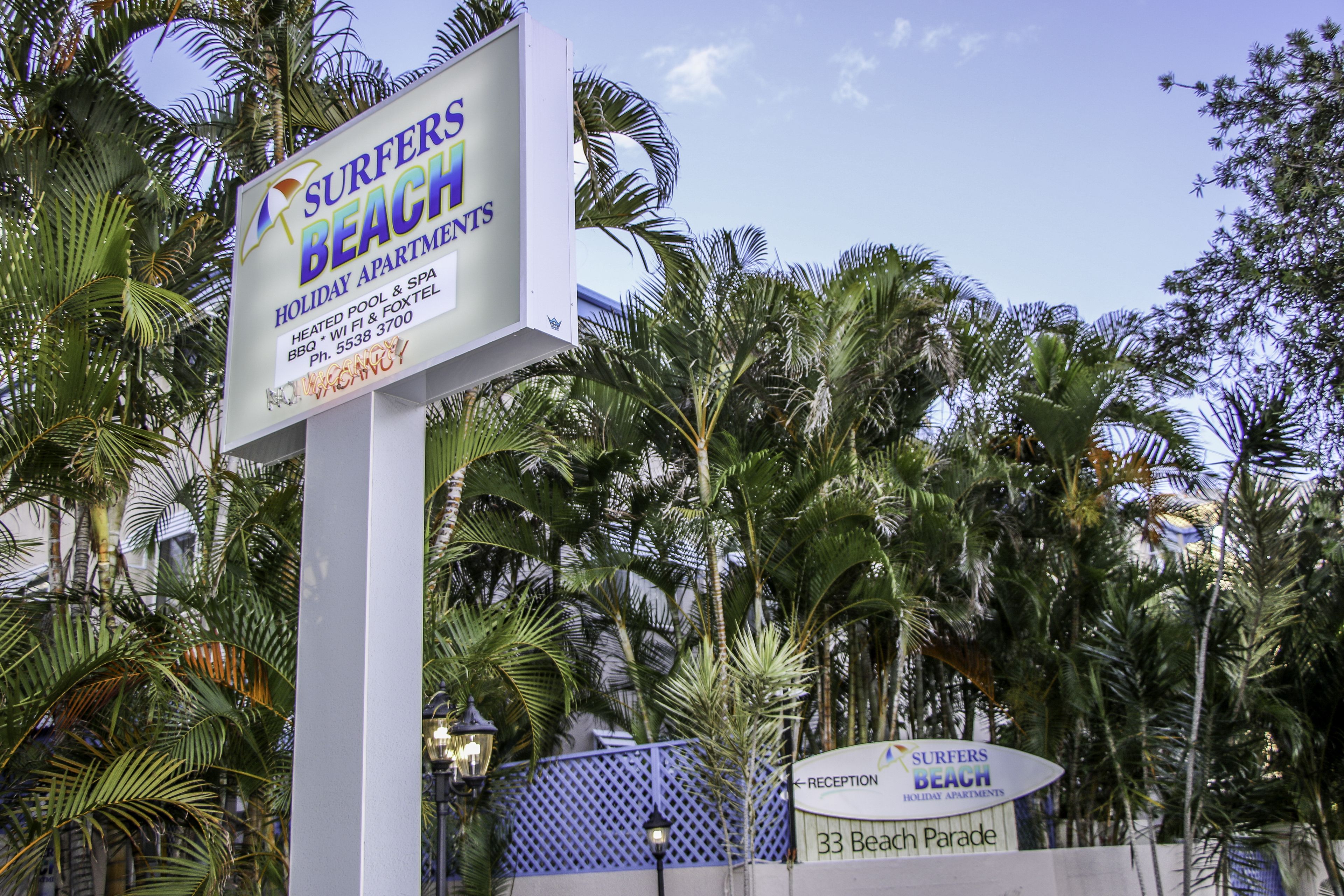 Surfers Beach Apartments -nimisen asuntokompleksin kyltti, jossa mainostetaan sen tarjoamia palveluita, kuten lämmitetty uima-allas, Wi-Fi ja grilli.