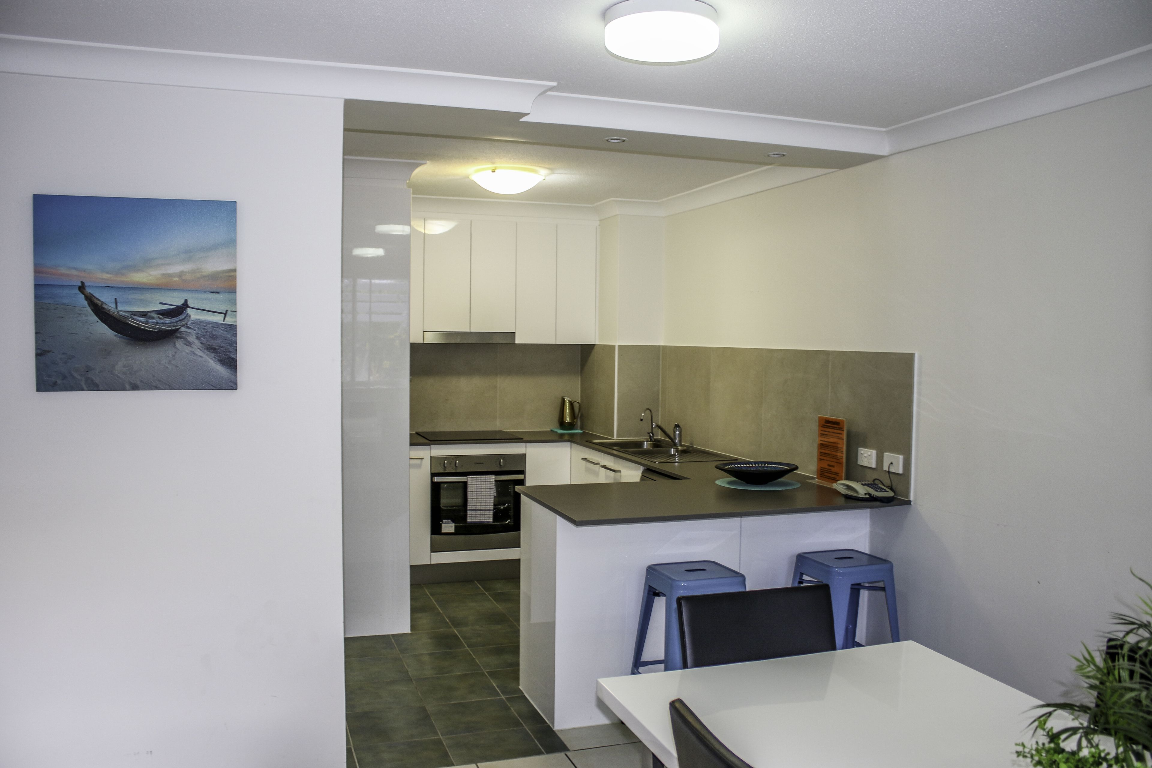 Een moderne keuken met witte kastjes, een centraal eiland en een eethoek met twee krukken.