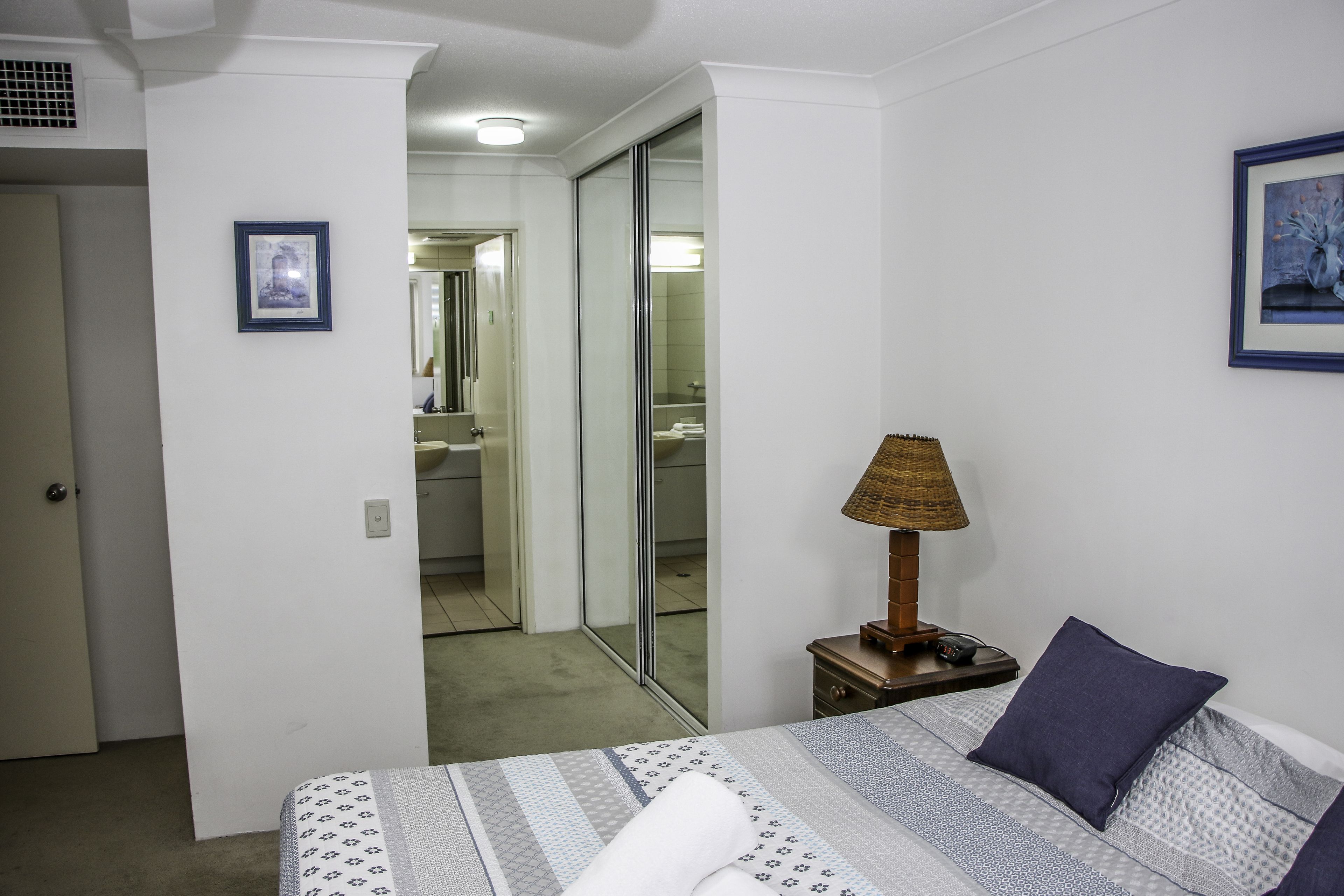 A bedroom with a bed, a nightstand, a lamp, and a framed picture on the wall.