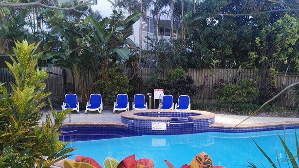 Piscina com azulejos azuis, rodeada por plantas tropicais e espreguiçadeiras azuis.