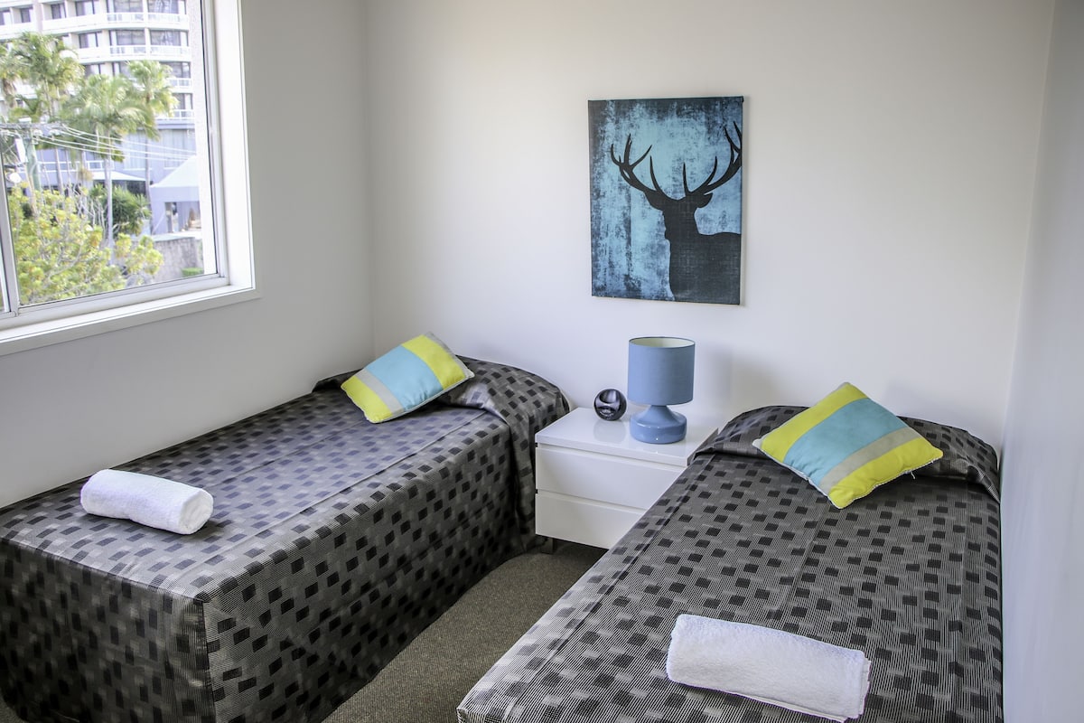A hotel room with two beds, a nightstand, a lamp, and a painting of a deer on the wall.