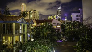 Um edifício com vários andares, varandas e um terraço no telhado, cercado por palmeiras e vegetação.