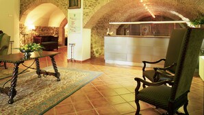 A lobby with a stone archway, a reception desk, a chandelier, and a dining area with a table and chairs. - Parador de Santo Domingo Bernardo de Fresneda (Santo Domingo de la Calzada)