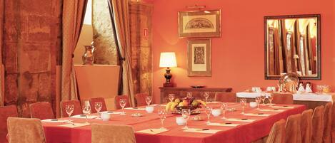 A long dining table with chairs, a chandelier, and a mirror on the wall.