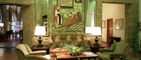 Una habitación tradicional con un gran tapiz, cuatro sillones, una mesa de centro de madera y un suelo con alfombra estampada.