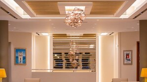 A modern lobby with a central chandelier, seating area, and artwork on the walls. - Lagas Aegean Village (Kos Town)