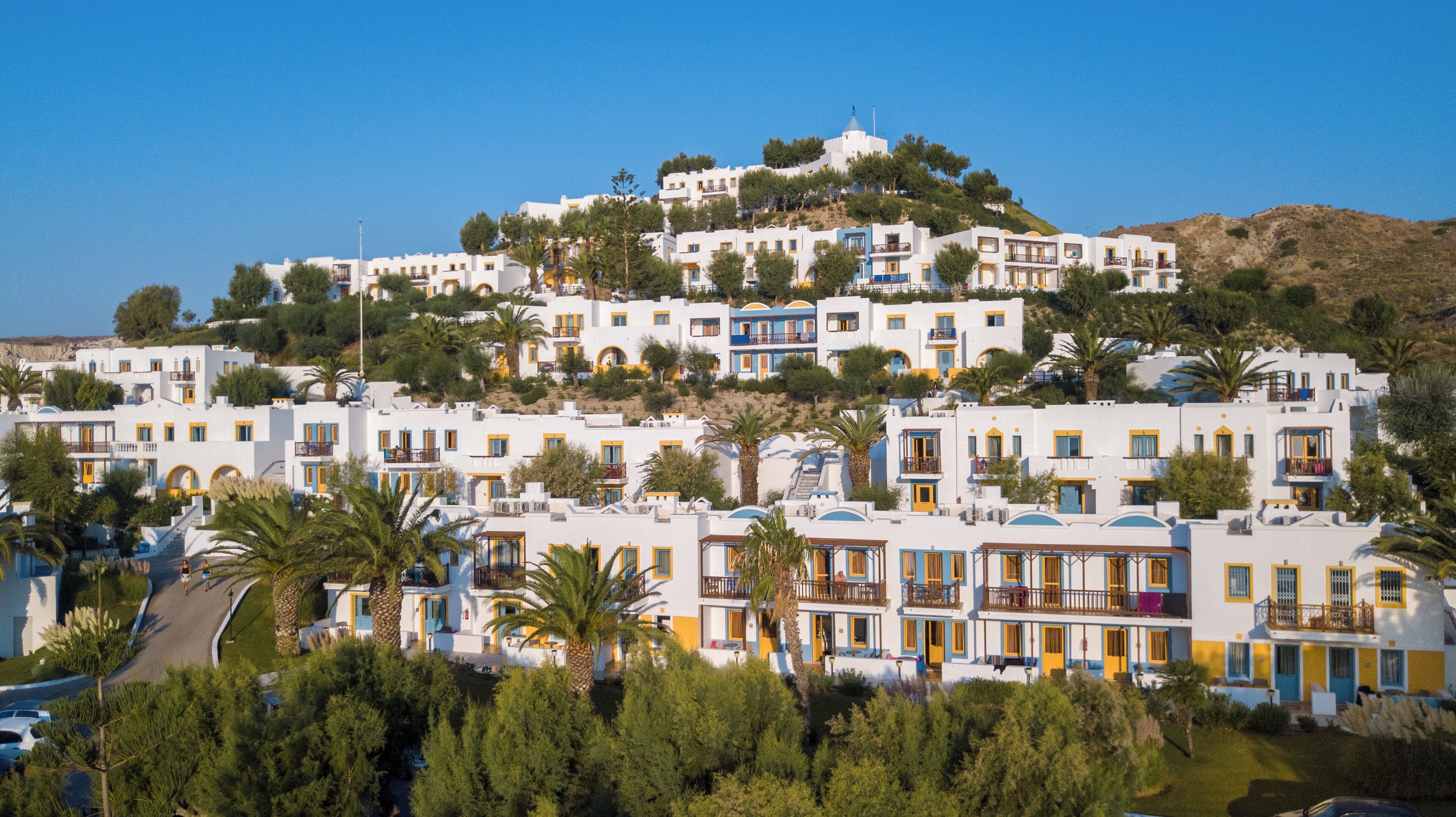 A hillside residential area with white buildings, balconies, and greenery.