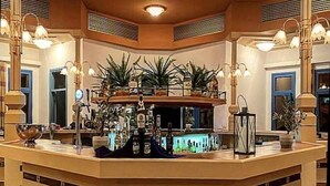 A bar area with a hexagonal ceiling light, a counter with bottles, and potted plants. - Lagas Aegean Village (Kos Town)