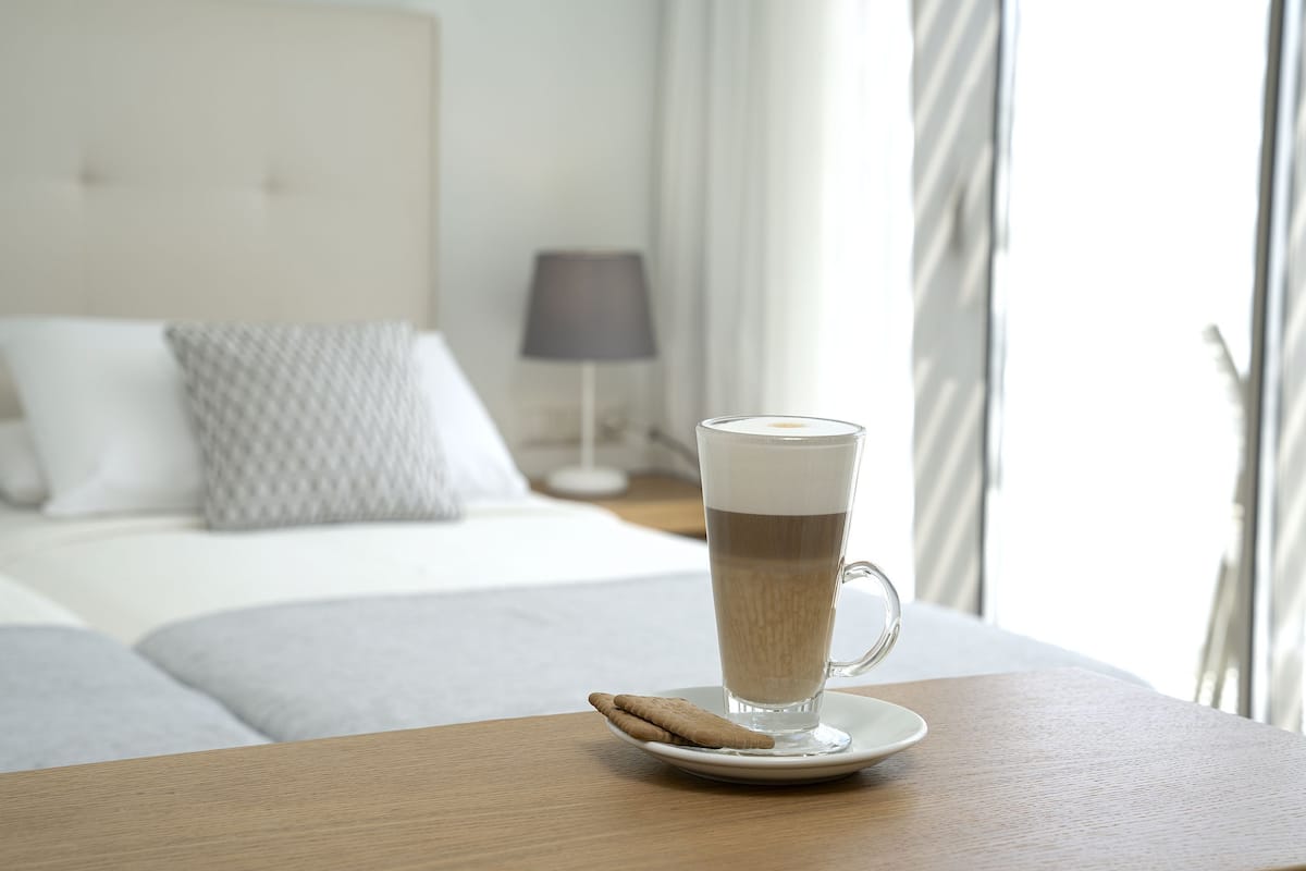 Una taza de café transparente sobre un plato con una galleta en una mesa de madera en una habitación de hotel.