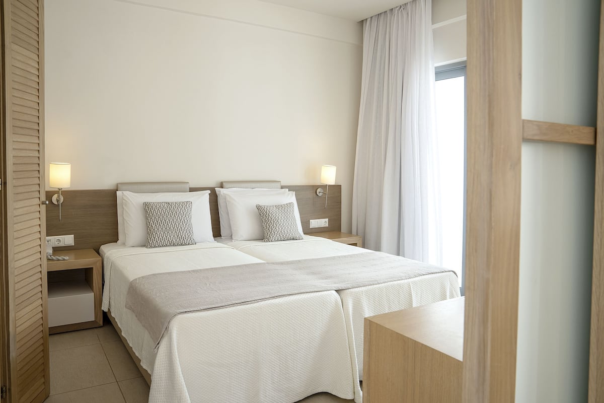 Una habitación de hotel con una cama doble, mesitas de noche, lámparas y una ventana con cortinas.
