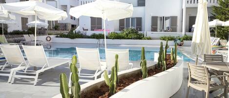 Un espace piscine agrémenté de chaises longues blanches, de parasols et de cactus.