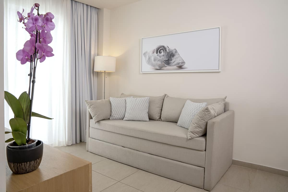 Una sala de estar moderna con un sofá beige, cojines estampados, una orquídea en maceta, una obra de arte enmarcada y una lámpara de pie.