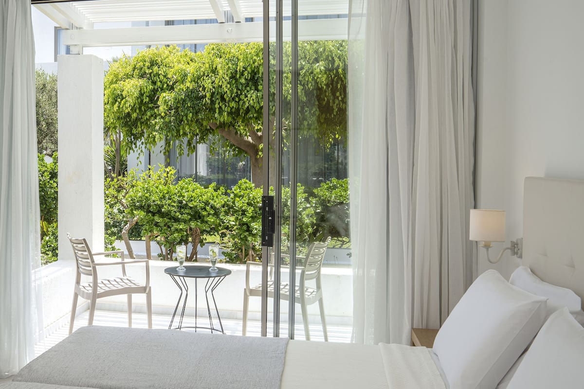 Una habitación de hotel con una cama, una pequeña mesa con sillas y vistas a zonas verdes.