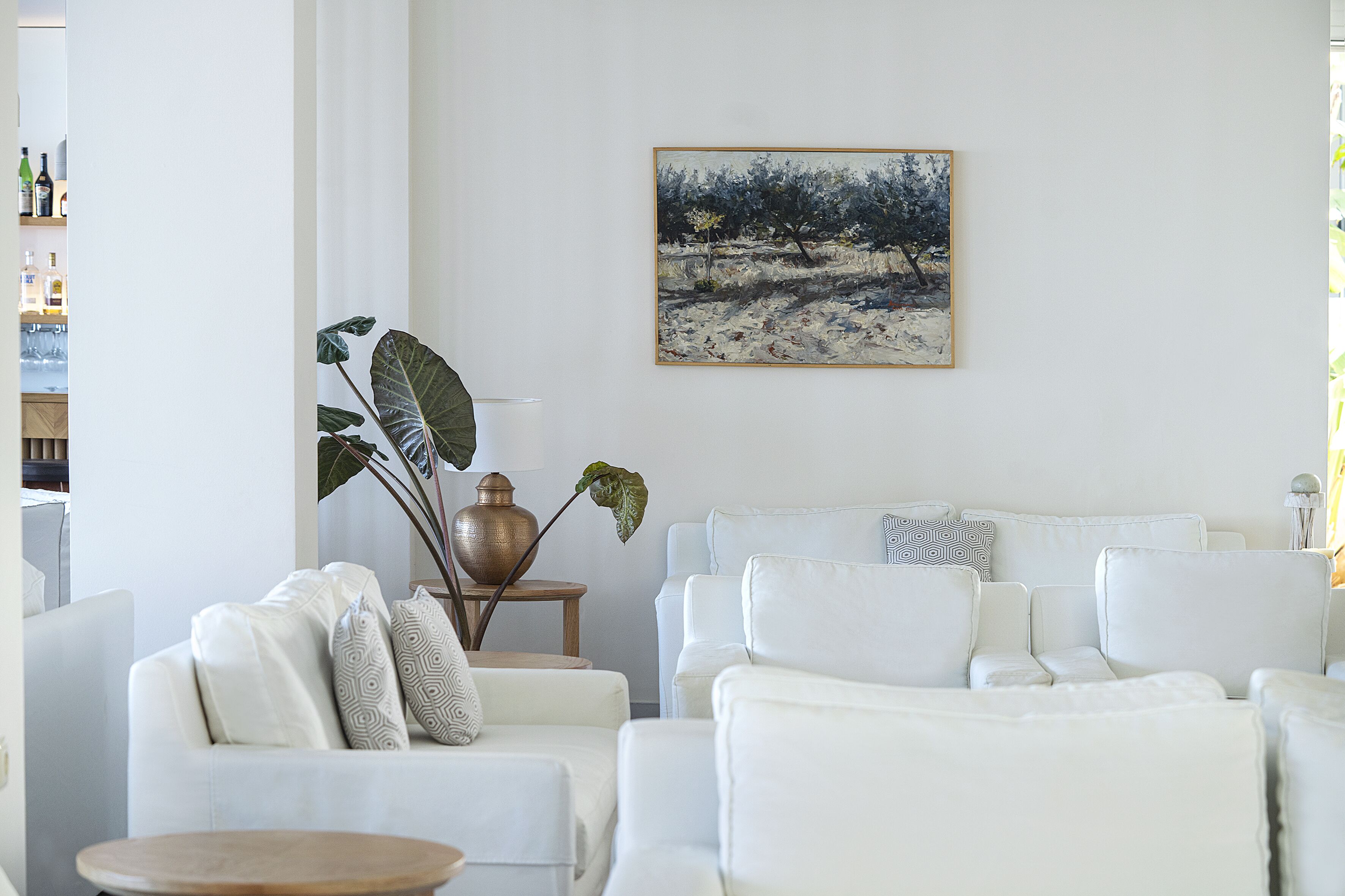 A modern living room with white furniture, a large painting, and a plant.
