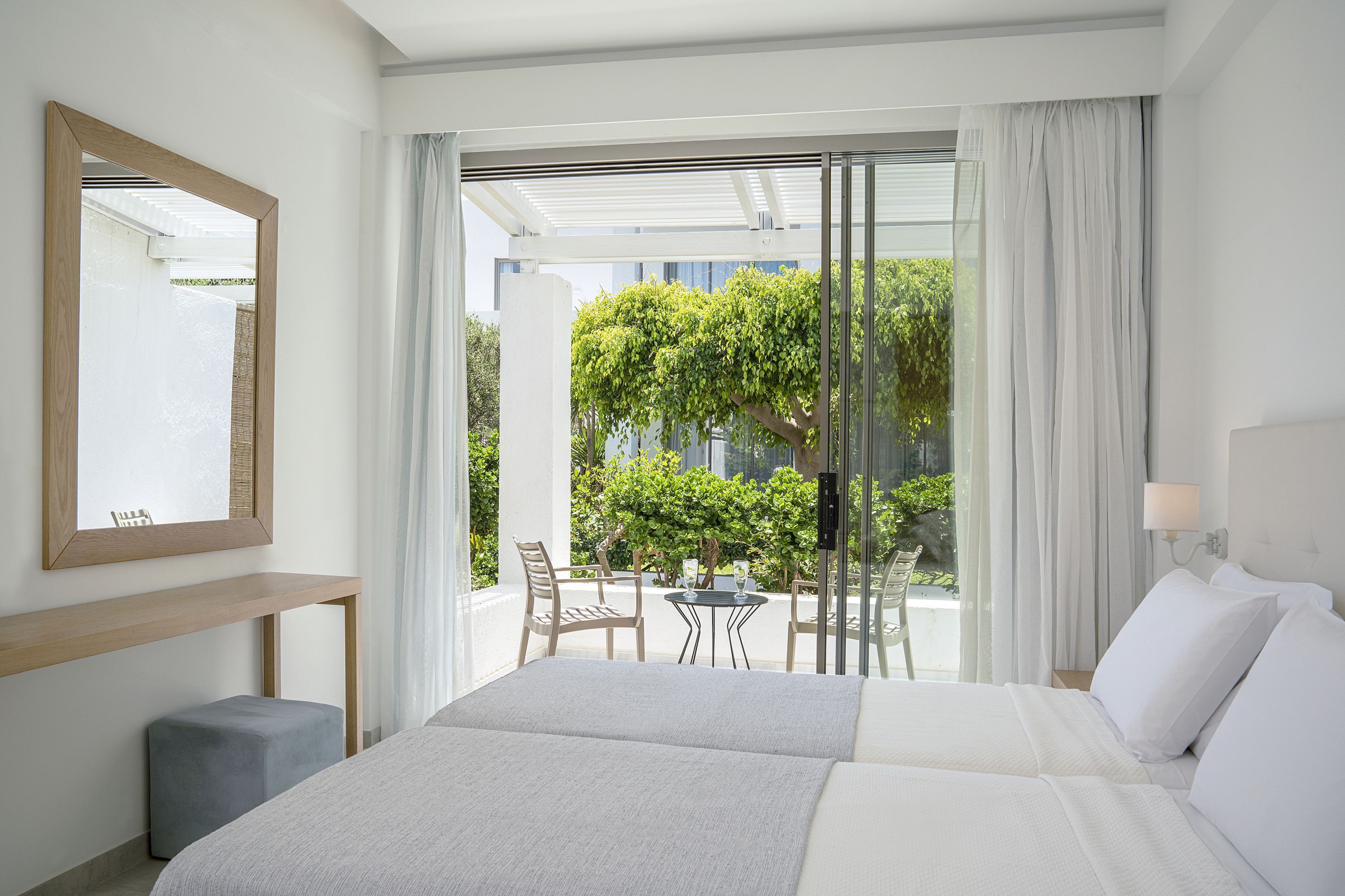 Habitación de hotel con una cama grande, una mesita, una silla, un balcón con vistas a zonas verdes y una ventana con cortinas.