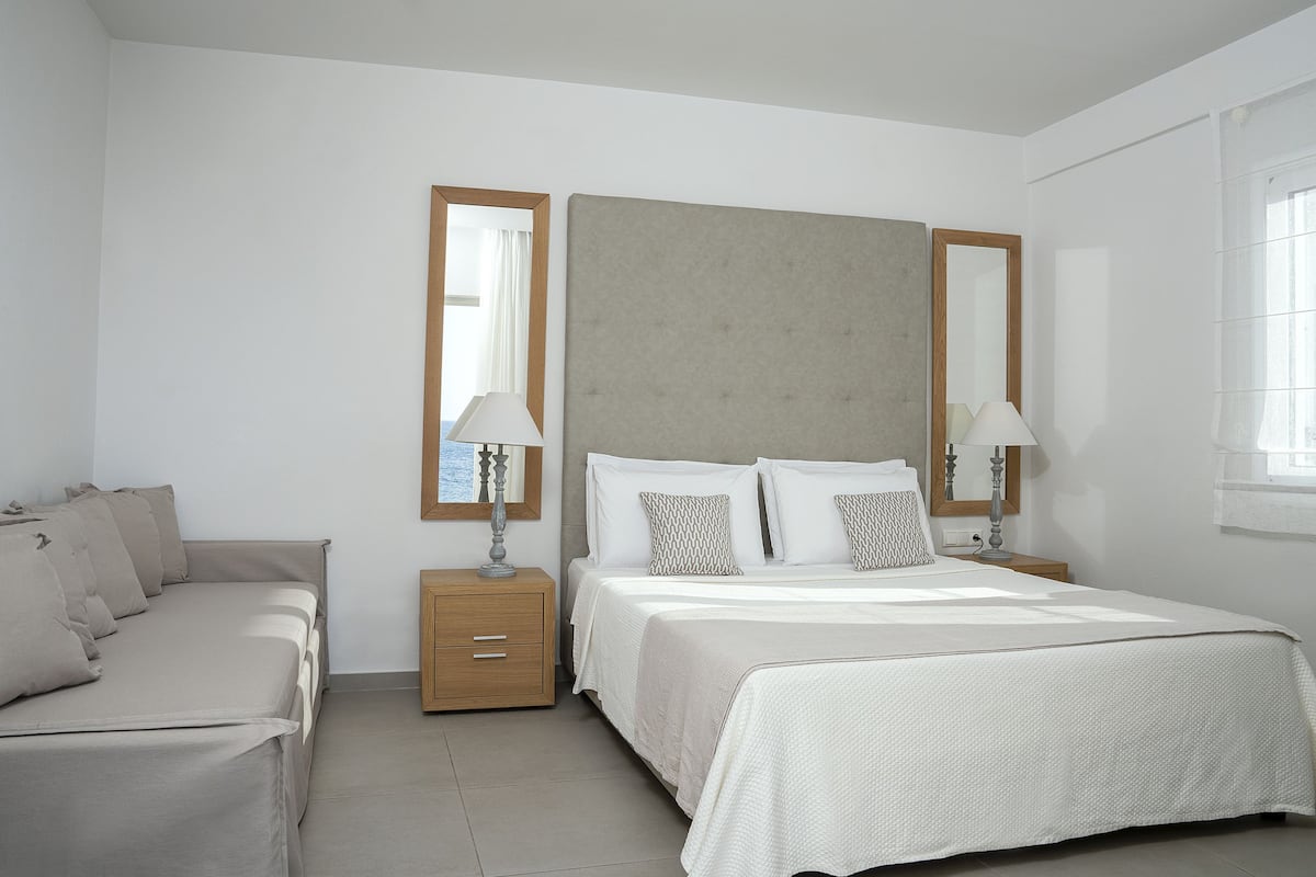 Un dormitorio con cama, mesita de noche, lámpara, espejo y ventana.