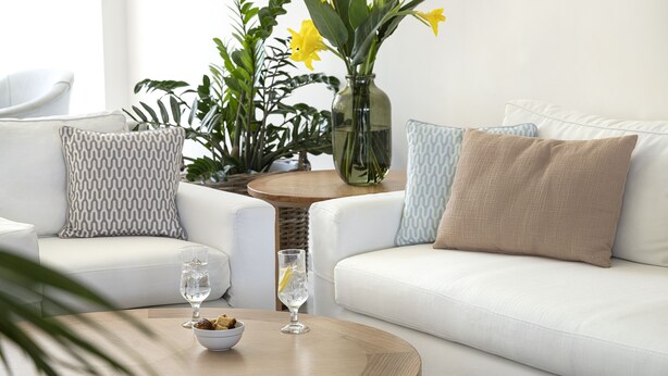 Un salon moderne avec un canapé blanc, des coussins à motifs, une table basse en bois et un vase rempli de fleurs jaunes.